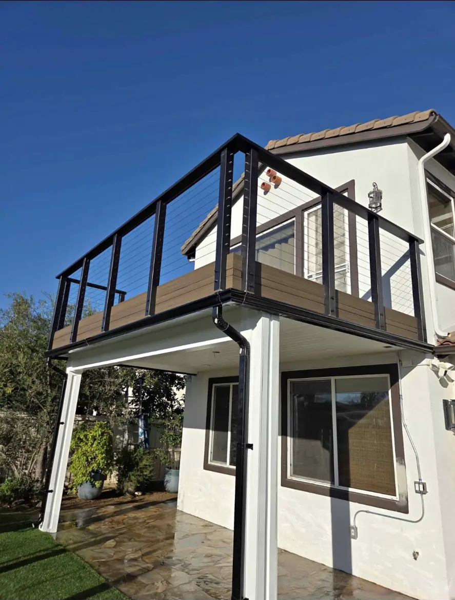 Second-story deck with black cable railing and composite boards over a stone patio